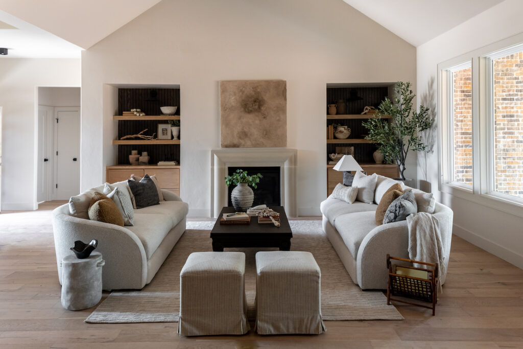 Symmetrical living room layout with matching curved sofas facing each other, a centered fireplace, built-ins, and a neutral modern palette