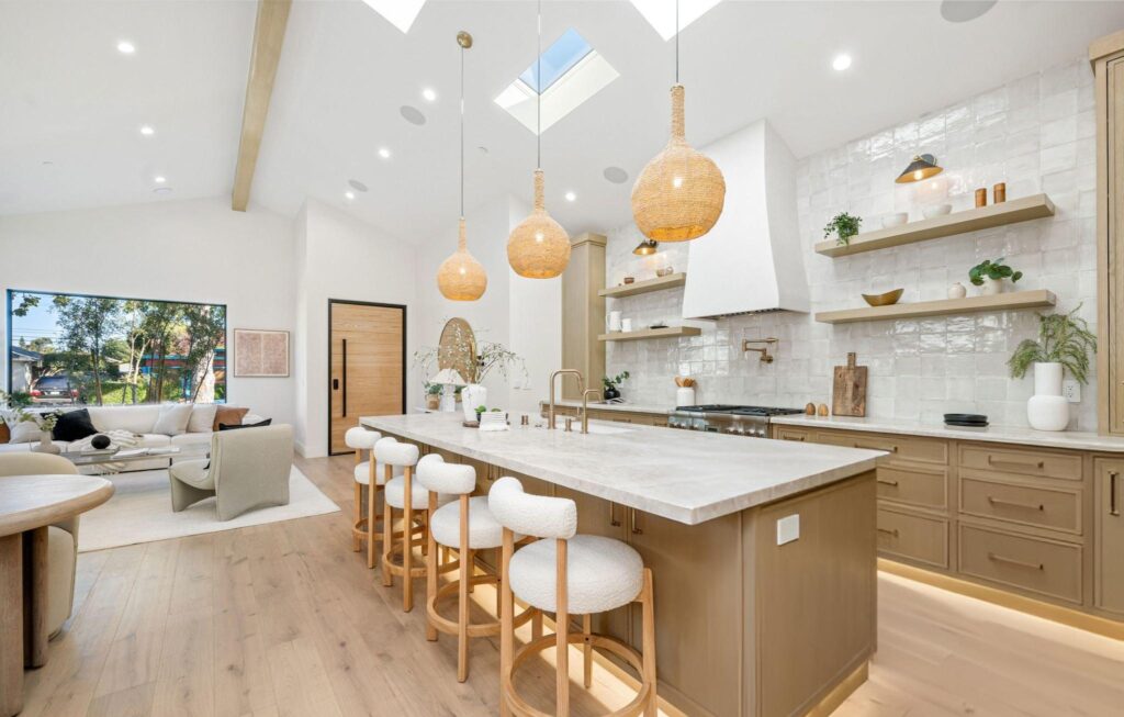 Bright open-concept kitchen with a long light oak island, woven pendant lights, white zellige backsplash, and seating that connects to the living area.