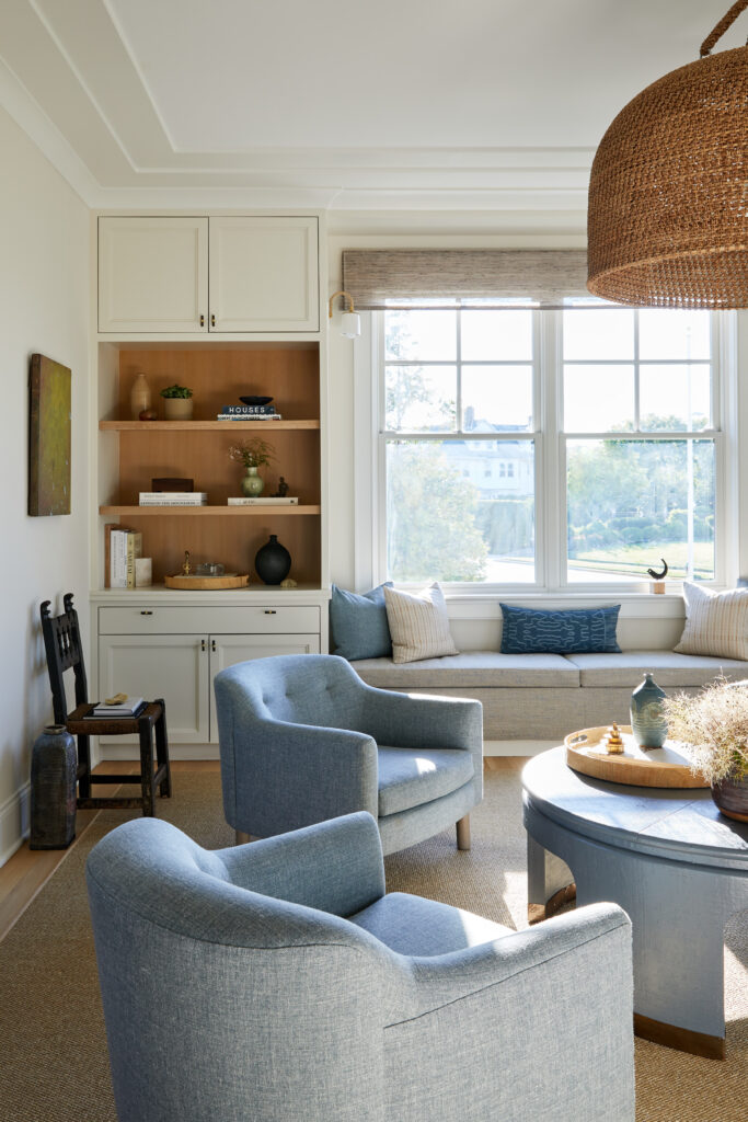 Cozy conversation nook with two blue swivel chairs, built-in shelves, and a window bench creating an intimate seating cluster in a bright living room.