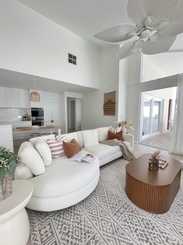 Open-concept living room with a curved white sectional, patterned rug, and warm wood accents creating a soft, defined seating zone.