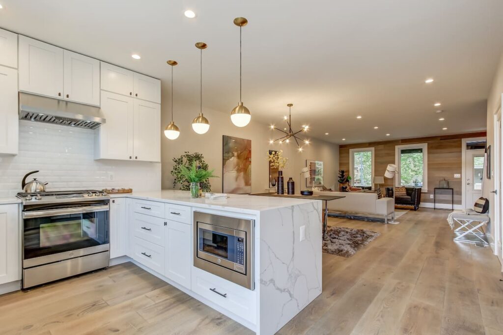 Open-concept kitchen and living layout with white cabinetry, marble island, brass pendant lighting, and seamless flow into a cozy modern living room.