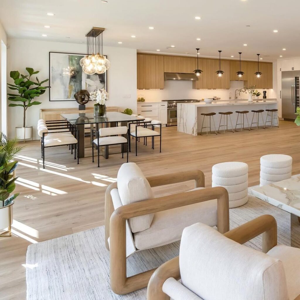 Bright modern open-concept living, dining, and kitchen space with light wood floors, a marble waterfall island, cozy neutral seating, and organic décor accents showing clear zoning and designer layout flow.