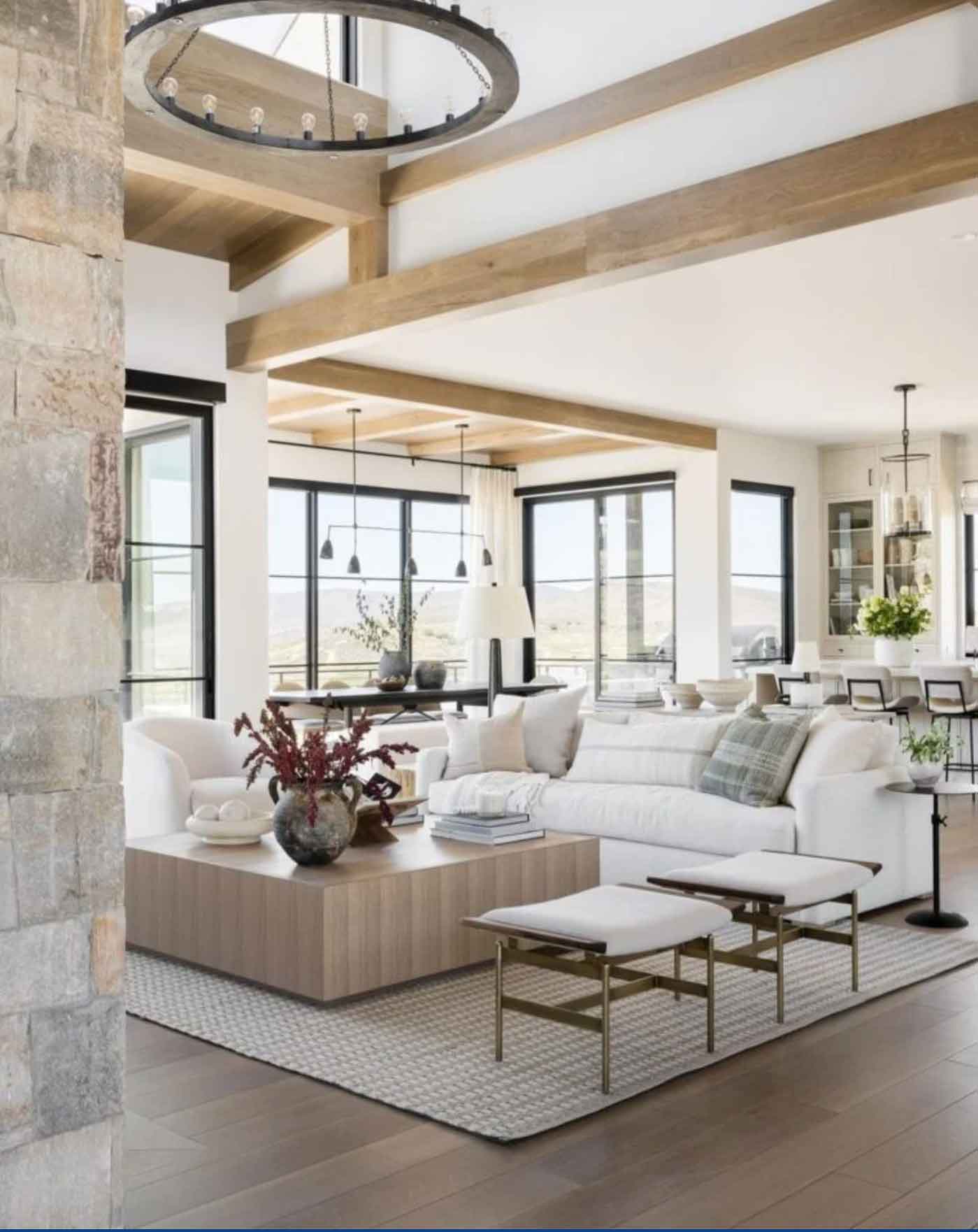 Open-concept living room with wood ceiling beams, a white sofa, large windows, and a neutral organic-modern layout connecting to the dining area.