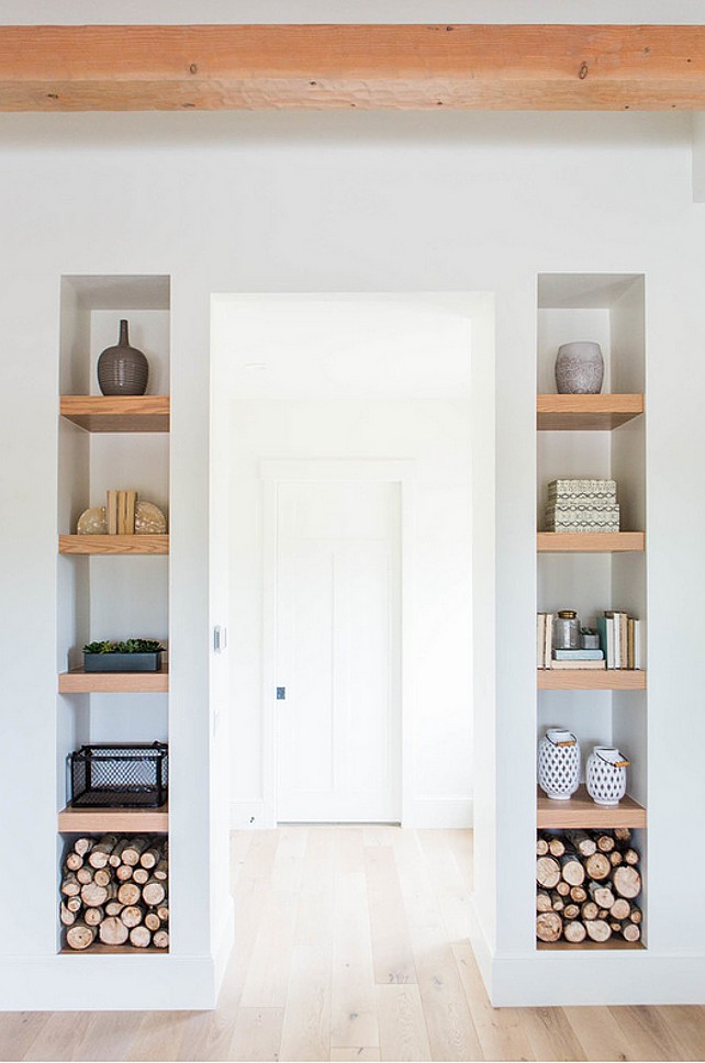 Built-in shelving flanking a hallway with natural wood shelves, minimal décor pieces, and stacked firewood for a clean and modern storage look.