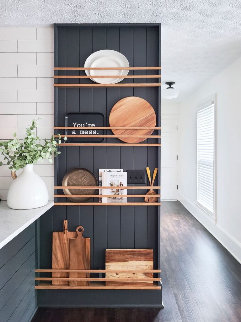 Dark shiplap accent shelving with wooden bars holding cutting boards, trays, and kitchen décor, creating a stylish open-storage display in a modern kitchen.