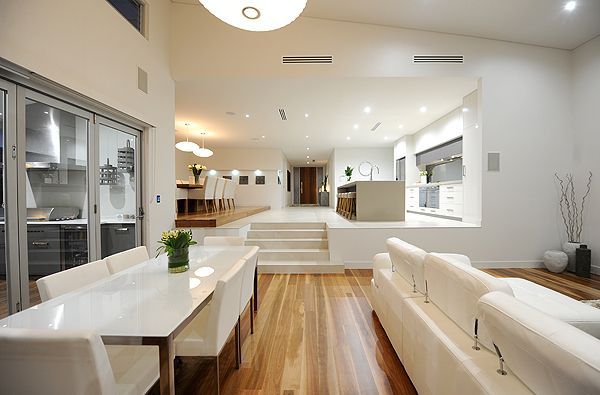 Modern split-level open-concept layout with white interiors, wood floors, and steps creating subtle separation between the living, dining, and kitchen spaces.