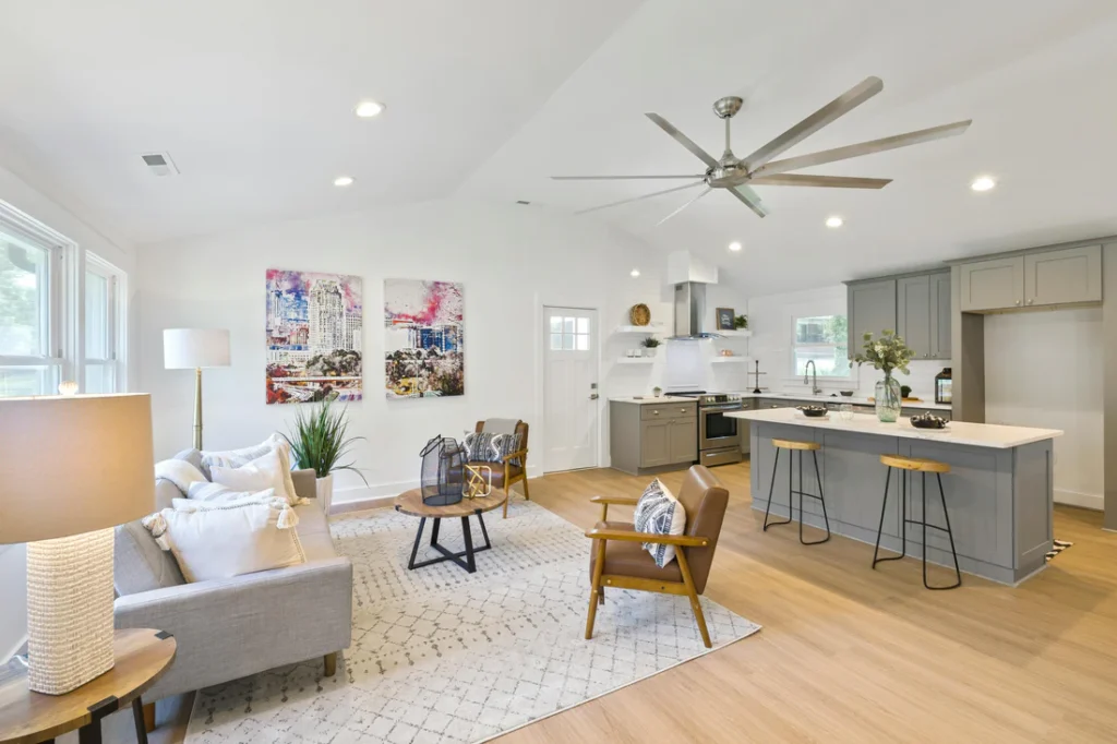 Bright open-concept living and kitchen space with a cozy seating area, gray island, and light wood floors creating clear functional zones.