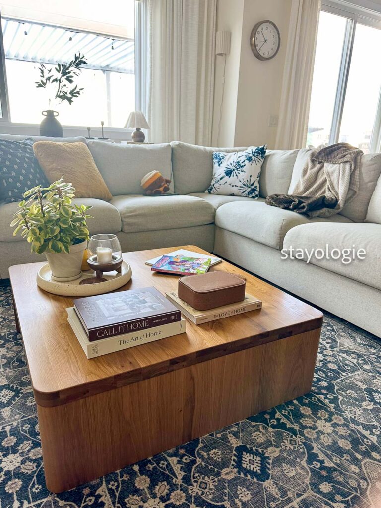Lived-in family living room with a neutral sectional sofa, children’s books and toys on a wooden coffee table, and soft natural light creating a calm, everyday home atmosphere.